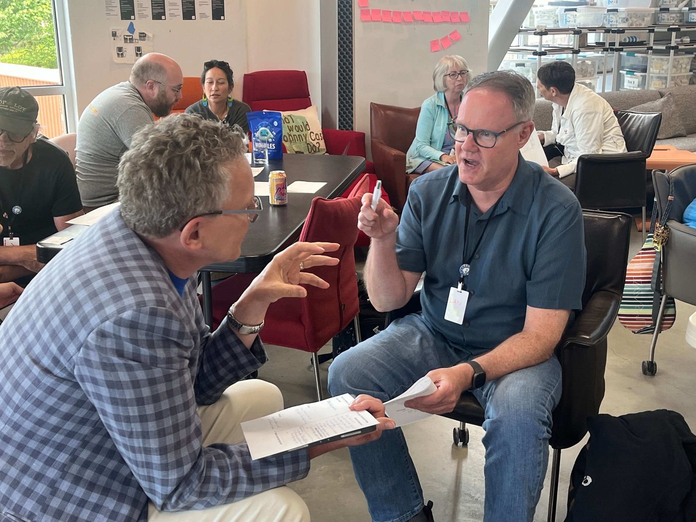 Two participants in an animated coaching conversation, sitting face to face with notes in hand.