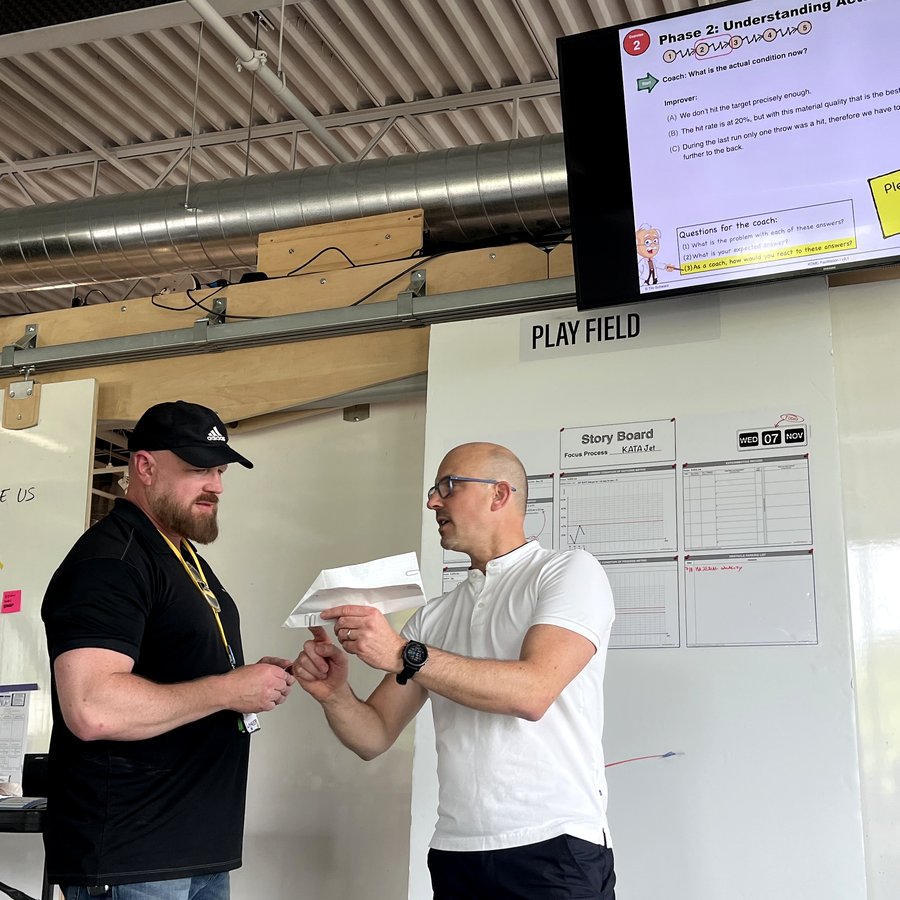 Two practitioners working through a Coaching Kata starter-question card during a coaching round.