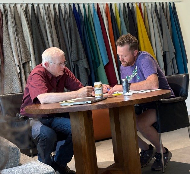 Two participants working in pairs at a small table, with the colorful Kaas Tailored fabric swatches lining the wall behind them.